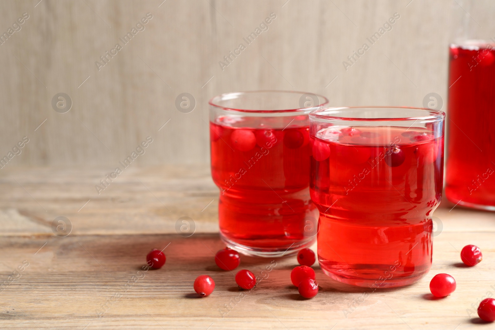 Photo of Tasty cranberry juice in glasses and fresh berries on wooden table, closeup. Space for text
