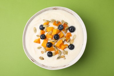 Photo of Bowl of delicious semolina pudding with blueberries, pumpkin and seeds on green background, top view