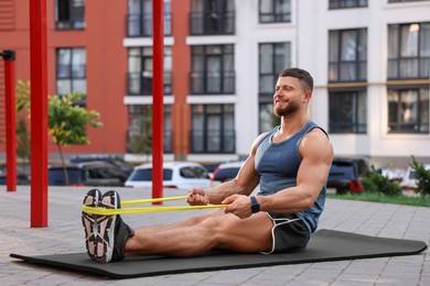 Photo of Muscular man doing exercise with elastic resistance band on mat at sports ground