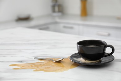 Photo of Cup and spilled coffee on white marble table in kitchen, space for text