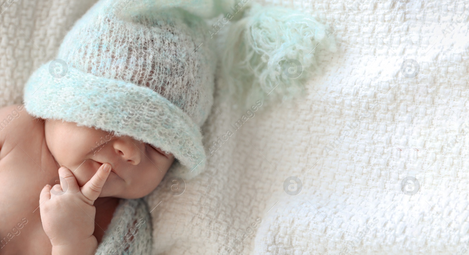 Image of Cute newborn baby in warm hat lying on white plaid, top view with space for text. Banner design