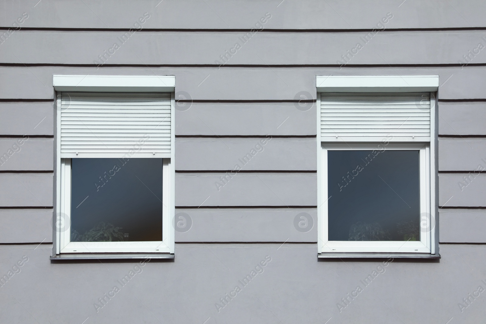 Photo of Wall of grey stone building with windows and rolling shutters