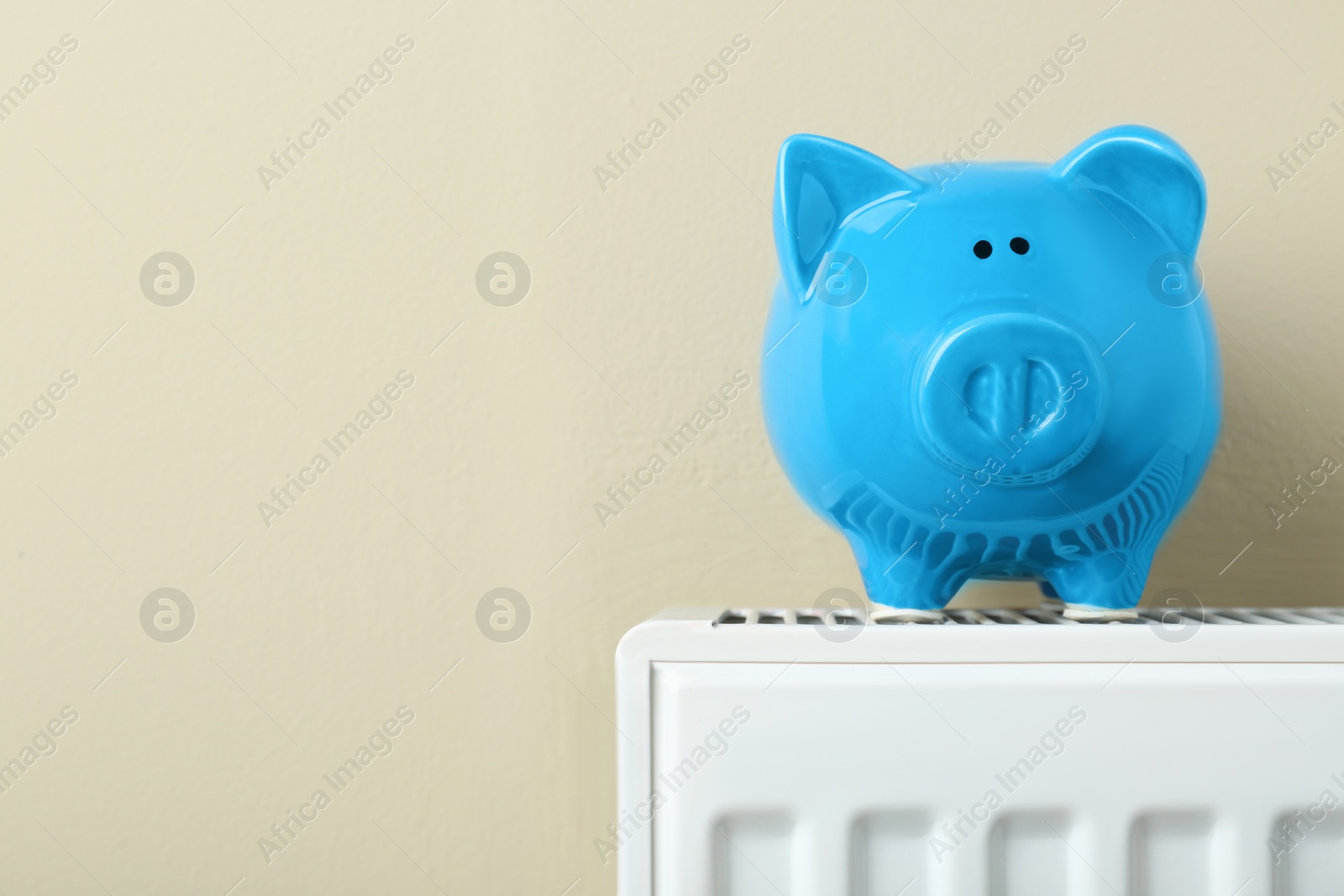Photo of Piggy bank on heating radiator against beige background, space for text
