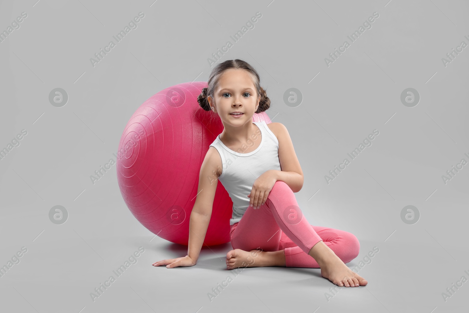 Photo of Cute little girl with fit ball on grey background