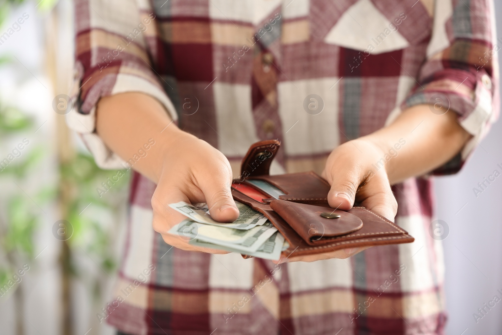 Photo of Woman putting money into wallet on blurred background, closeup