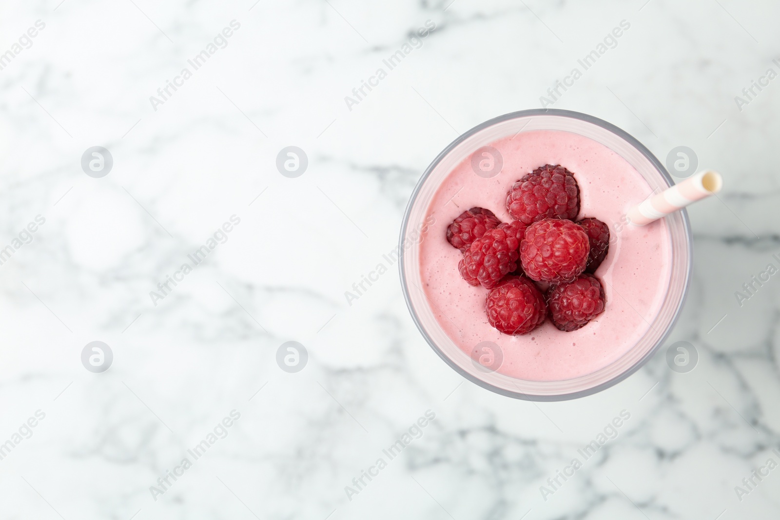 Image of Yummy raspberry smoothie in glass on white marble table, top view. Space for text 