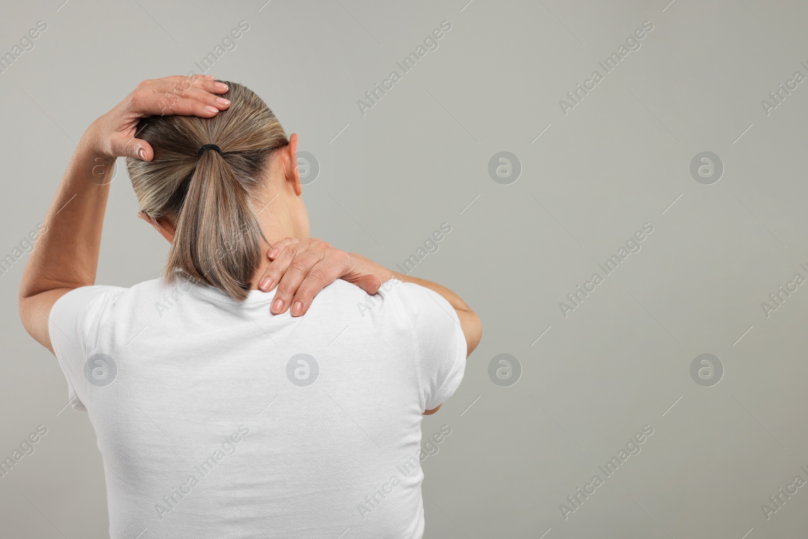 Photo of Mature woman suffering from pain in her neck on grey background, back view. Space for text