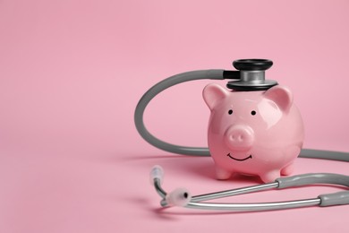 Photo of Piggy bank and stethoscope on pink background, space for text. Medical insurance