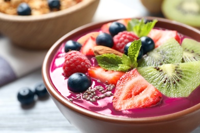 Photo of Delicious acai smoothie with chia seeds and fruits in dessert bowl served on white wooden table, closeup