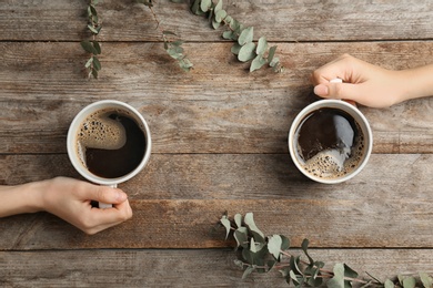 Photo of Young women with cups of delicious hot coffee on wooden background, top view