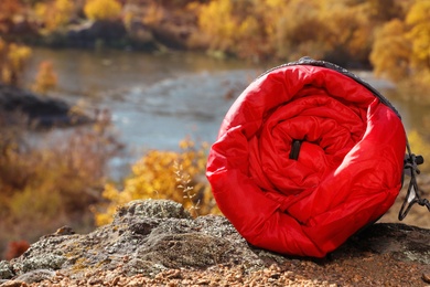 Photo of Red sleeping bag on rock outdoors, space for text. Camping equipment