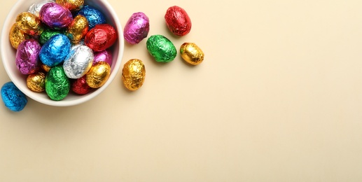 Chocolate eggs wrapped in colorful foil on beige background, flat lay. Space for text