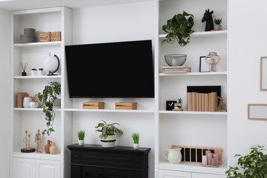 Photo of Stylish room interior with modern TV set and shelves with decor and houseplants