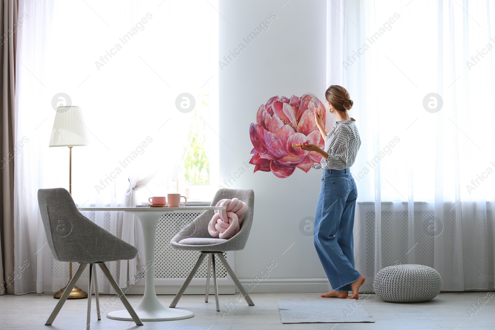 Photo of Young interior designer painting flower on wall in modern room