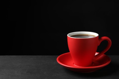 Red cup with aromatic coffee on black textured table. Space for text