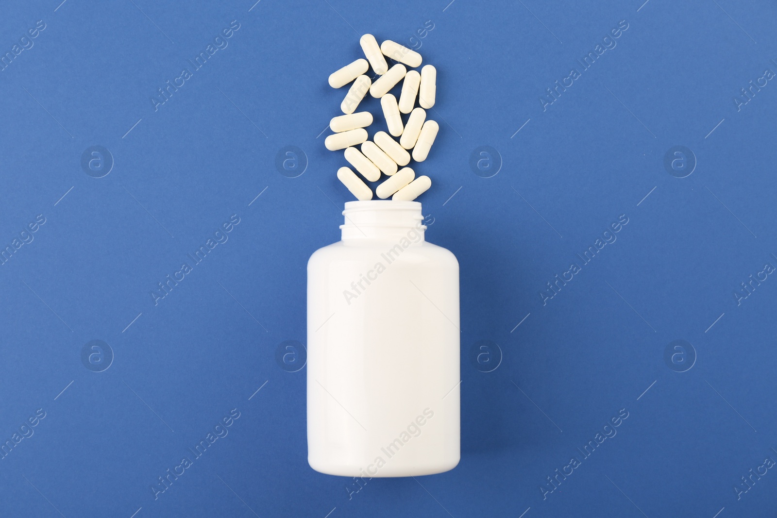 Photo of Bottle and vitamin capsules on blue background, top view