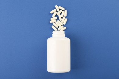 Bottle and vitamin capsules on blue background, top view