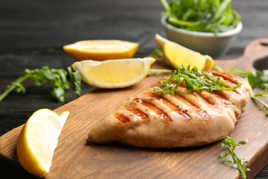 Photo of Tasty grilled chicken fillet with lemon and arugula on wooden board, closeup