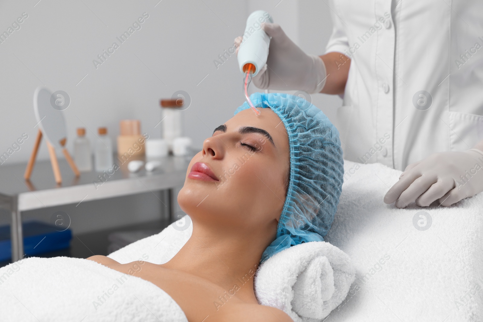 Photo of Young woman undergoing face rejuvenation procedure with darsonval in salon