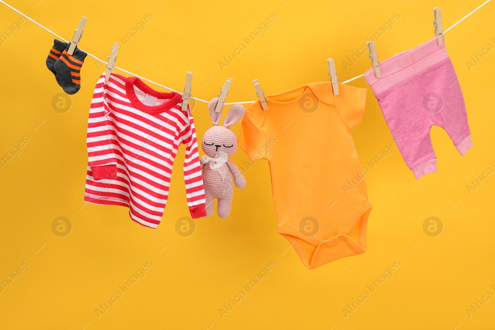 Photo of Different baby clothes and bunny toy drying on laundry line against orange background