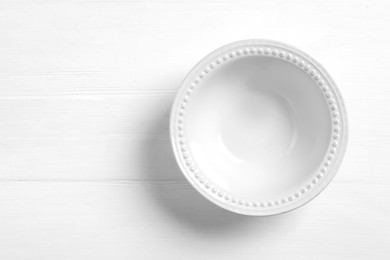 Photo of Empty ceramic bowl on white wooden table, top view. Space for text