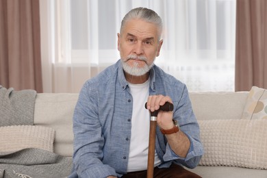 Senior man with walking cane sitting on sofa at home