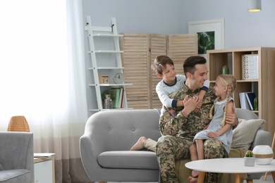 Young man in military uniform with his children on sofa at home