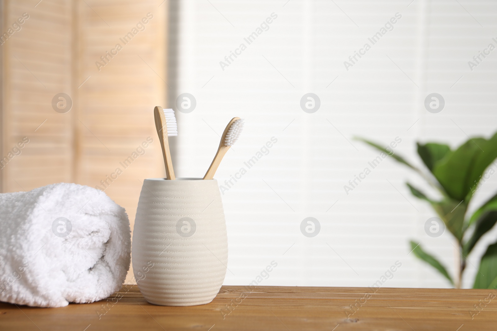 Photo of Holder with bamboo toothbrushes and towel on wooden table in bathroom, space for text