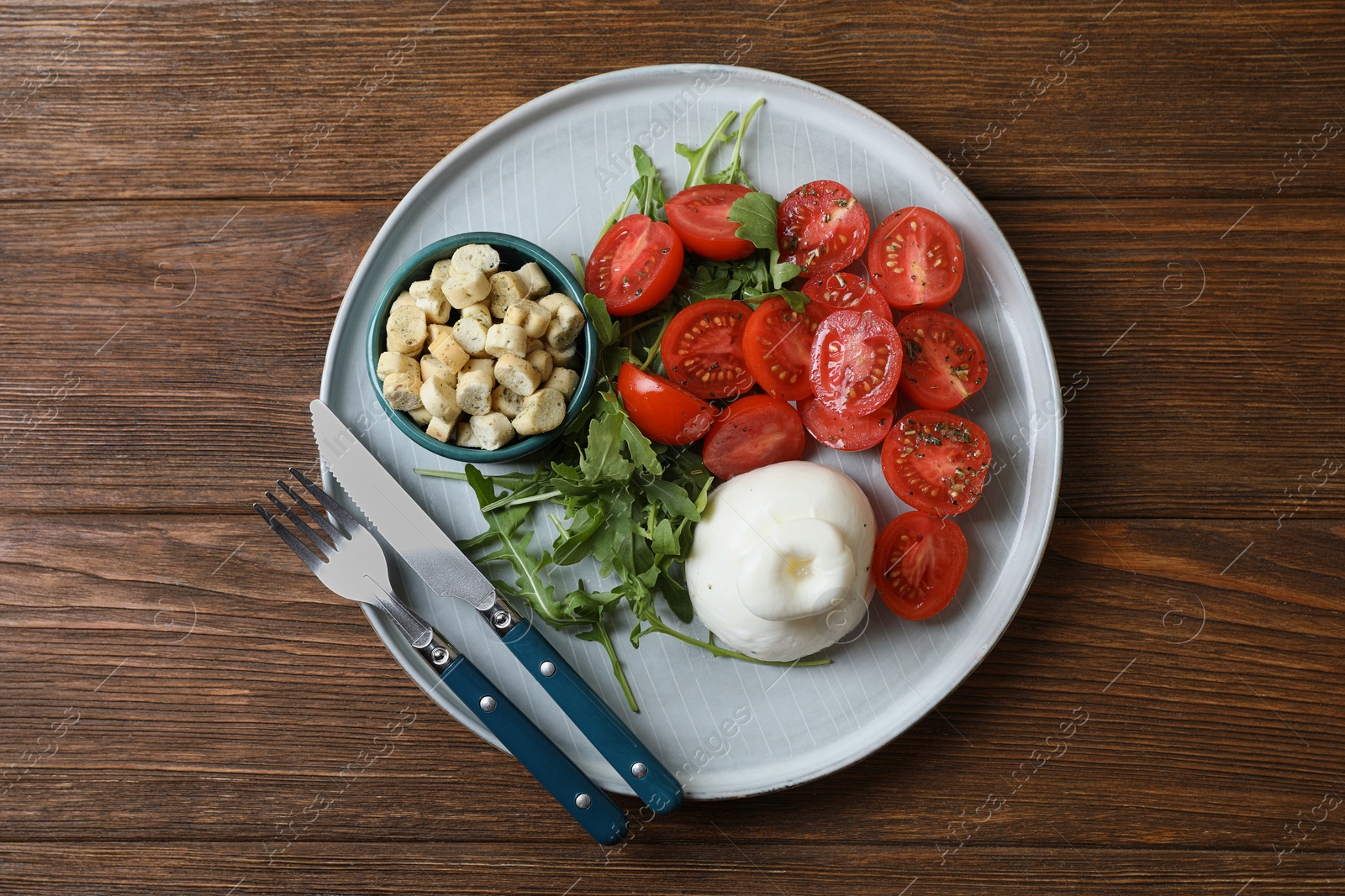 Photo of Delicious burrata cheese with tomatoes and arugula served on wooden table, top view