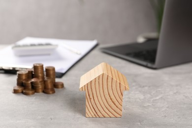 Photo of House model, stacked coins, laptop and clipboard on grey table, selective focus