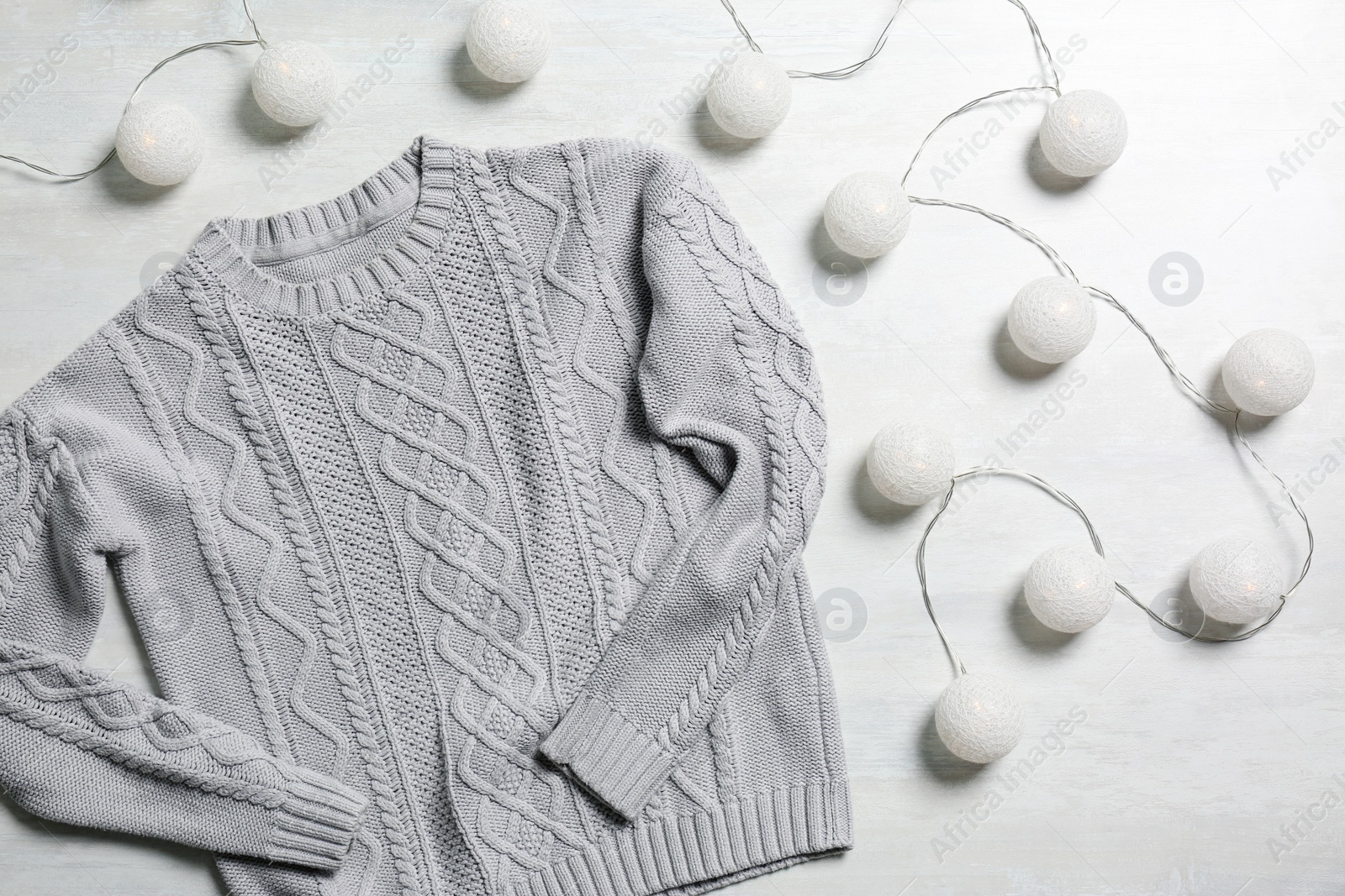 Photo of Flat lay composition with warm sweater and fairy lights on light background