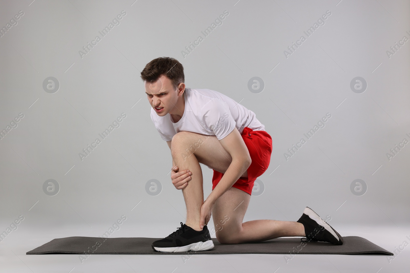 Photo of Man suffering from leg pain on mat against grey background