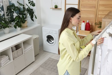 Beautiful young woman taking shirt from rack in laundry room