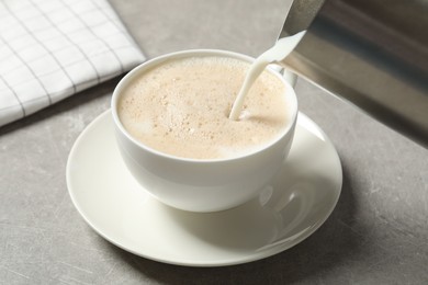 Pouring milk into cup of coffee on grey table