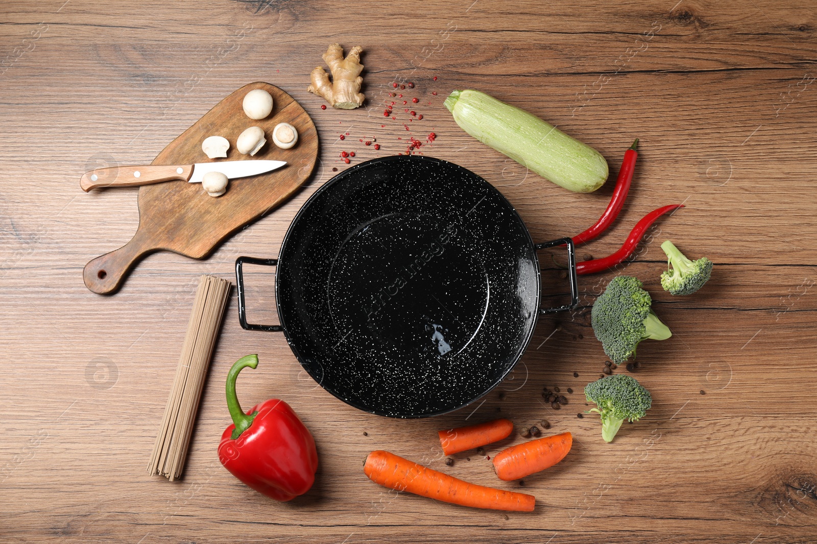 Photo of Empty iron wok surrounded by raw ingredients on wooden table, flat lay