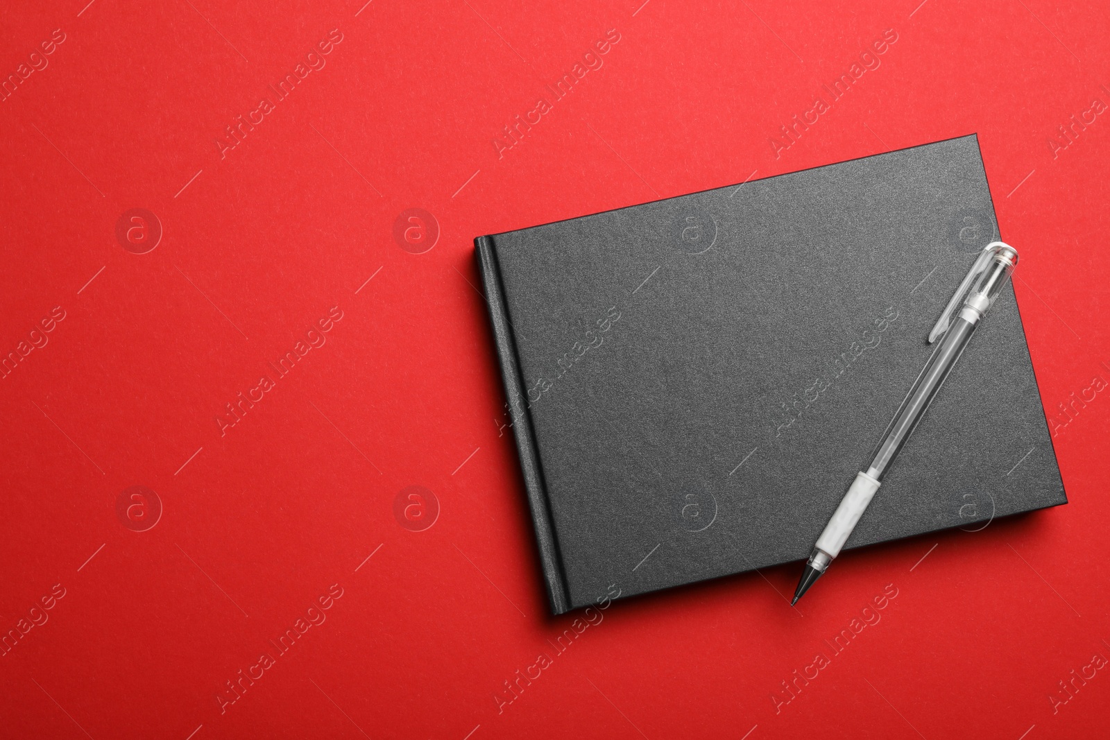 Photo of Stylish black notebook and pen on red background, top view. Space for text