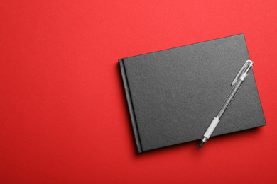 Photo of Stylish black notebook and pen on red background, top view. Space for text
