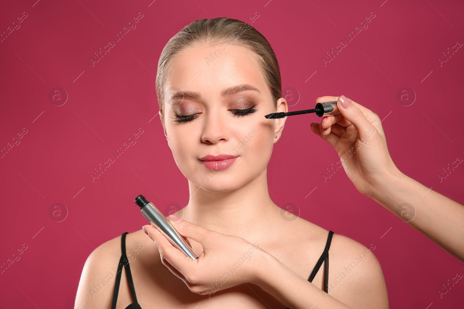 Photo of Artist applying makeup onto woman's face on pink background