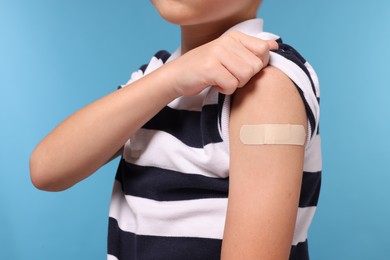 Boy with sticking plaster on arm after vaccination against light blue background, closeup