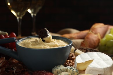 Fondue pot with tasty melted cheese, fork and different snacks on table