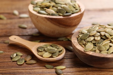 Bowls and spoon with peeled pumpkin seeds on wooden table, closeup