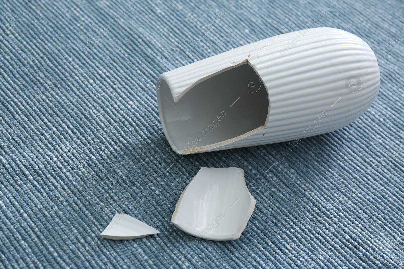 Photo of Broken white ceramic vase on grey carpet, closeup