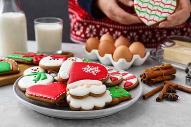 Photo of Woman holding delicious homemade Christmas cookie at grey marble table, focus on plate