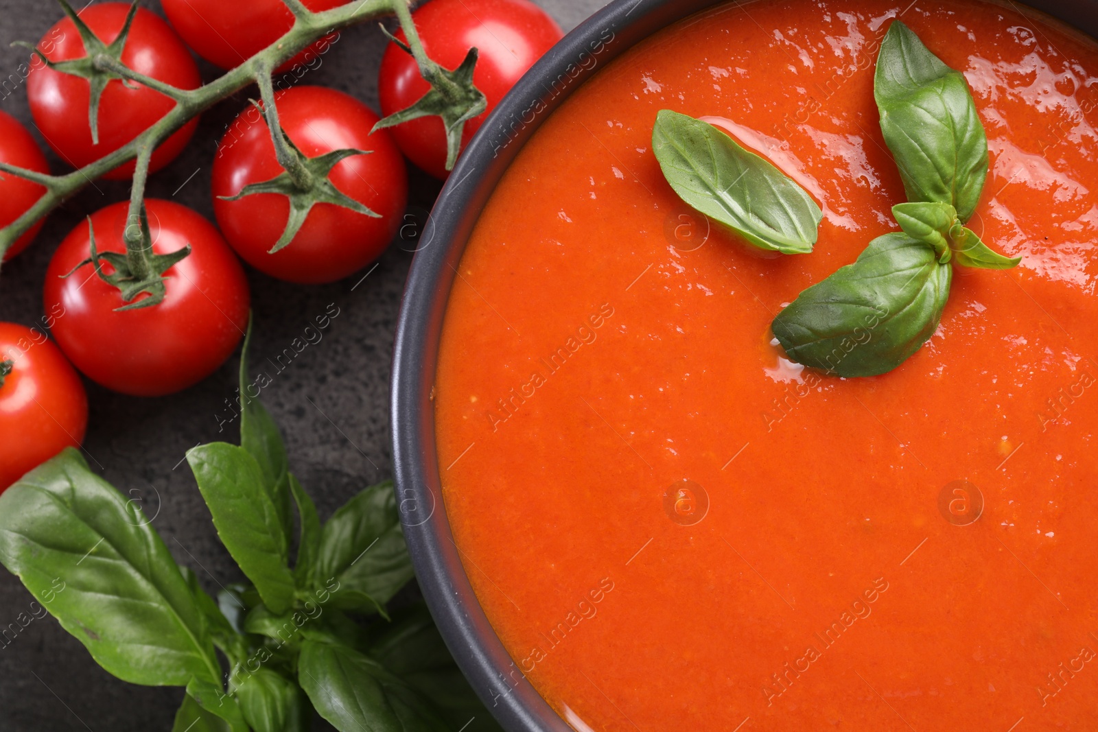 Photo of Delicious tomato cream soup in bowl and ingredients on grey table, flat lay