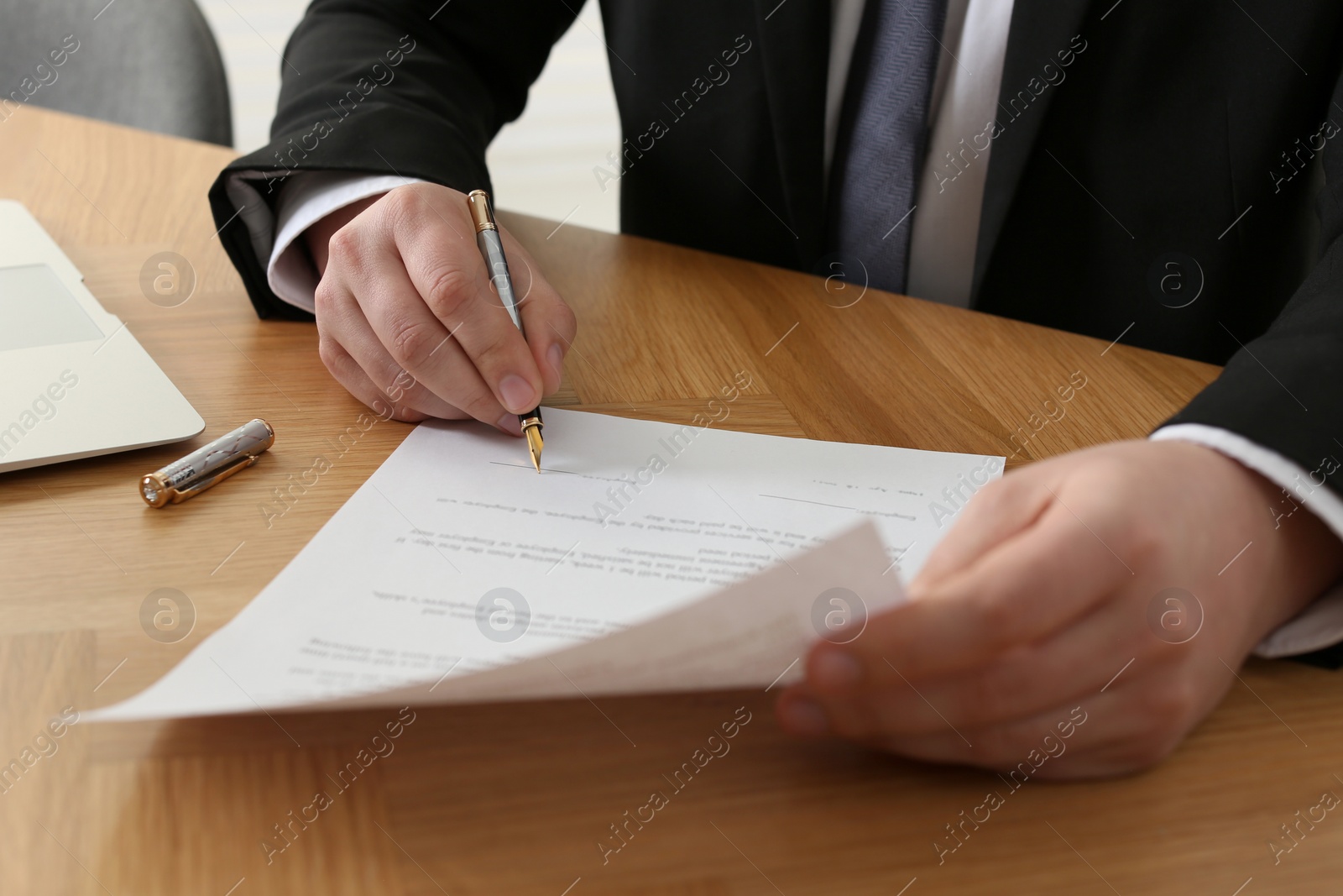 Photo of Notary signing document at wooden table, closeup