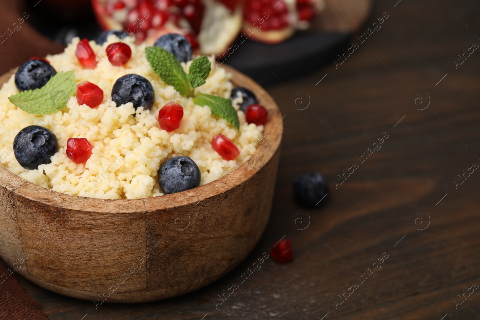 Photo of Bowl of tasty couscous with blueberries, pomegranate and mint on wooden table, closeup. Space for text