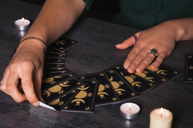 Photo of Soothsayer predicting future with tarot cards at table in darkness, closeup