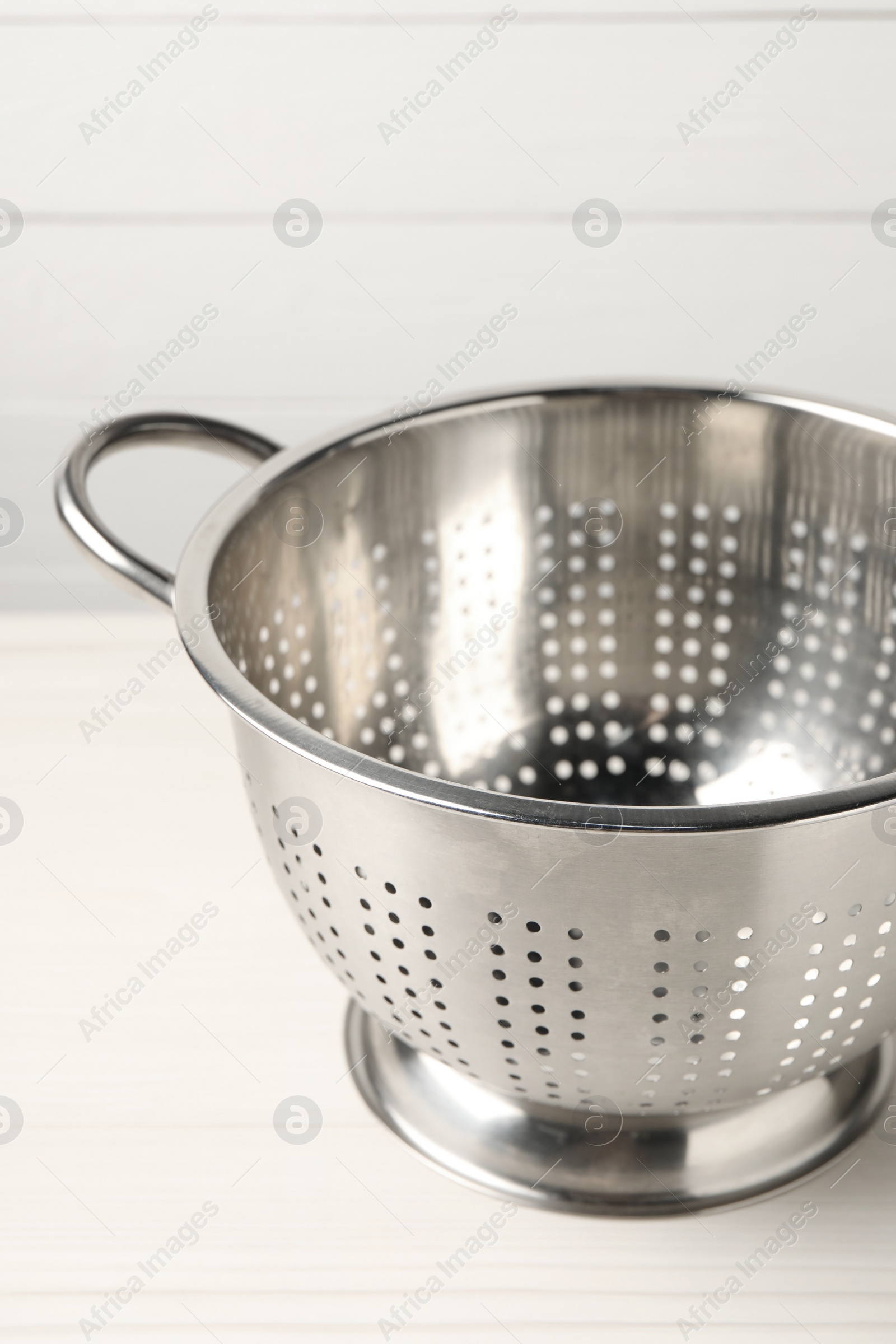 Photo of One metal colander on white wooden table