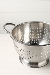 One metal colander on white wooden table