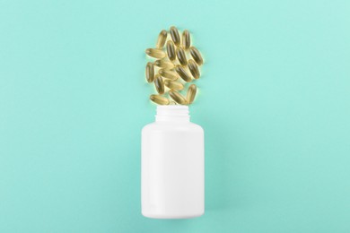 Bottle and vitamin capsules on turquoise background, top view